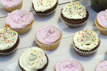 vanilla muffin with pink cream lies on a white wooden table on the background of other muffins