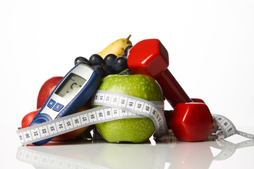 Blood sugar control glucometer for glucose level with healthy organic food and dumbbells with measuring tape on a white background. Healthy lifestyle, detox, weight loss and Diabetes concept