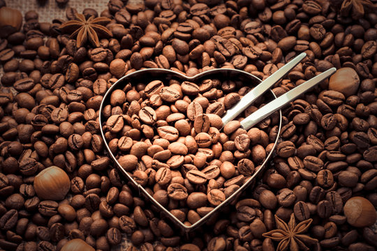 Heartwarming. Coffee beans and nuts background with a metal heart shape in a middle - top view