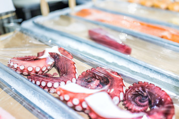 Macro closeup of many fresh cooked purple red octopus legs in seafood market store shop wrapped in plastic on display
