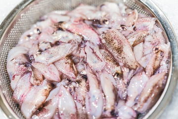 Macro closeup of many raw slimy purple squid cut in sieve cold on ice preparation