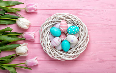  Easter eggs in a wicker basket and bouquet tulips on wooden background.Easter holiday concept.