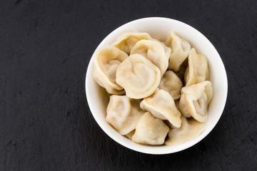 Traditional russian pelmeni, ravioli, dumplings with meat on black  stone background . Copyspace