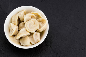 Traditional russian pelmeni, ravioli, dumplings with meat on black  stone background . Copyspace