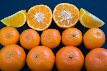 Bright mandarins are harmoniously lying on a dark blue background. Slices of citrus and peel.