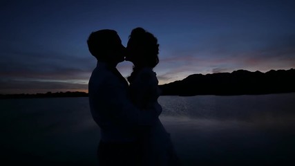 Dark silhouettes of the bride and groom on a tropical ocean beach at sunset. Sensual hugs and kisses.