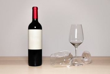 red wine bottle composition with two glasses on wood with gray white background and blank label