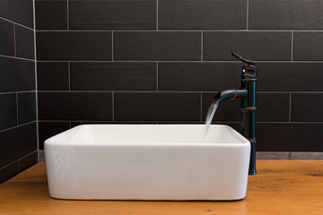Modern white square sink in bathroom with black tiles and black faucet in shape of bamboo. Modern...