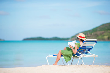 Young woman reading book on chaise-lounge on the beach