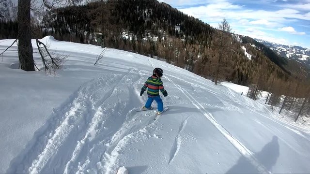 Freeride skiing. Little boy skiing in the wild. Skiing down. A 5 year old child enjoys a winter holiday in the Alpine resort. Stabilized shot. Slow motion.
