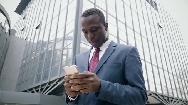 young afro american businessman in the street types on his smartphone