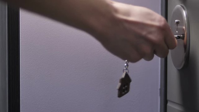 Close-up slow motion shot of female hand holding door keys with wooden house shaped key ring. Woman locking or unlocking door of her house or apartment.