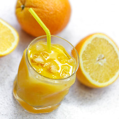 Glass of freshly squeezed orange juice with ice on a light gray background