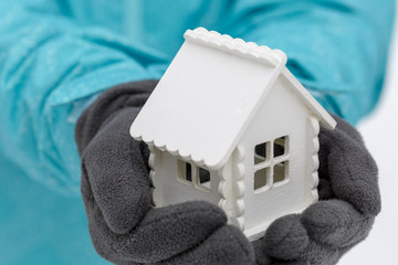 White toy house lies in the hands of a man wearing dark gloves in the winter