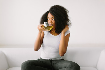 An African American young woman sitting in the lotus position on white bed with cup of tea