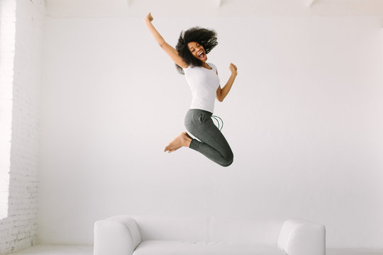 An African American Young Woman Jumping On White Bed