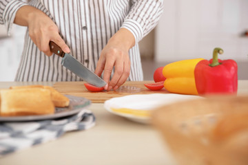 Woman cutting tomato for tasty toast on board at table