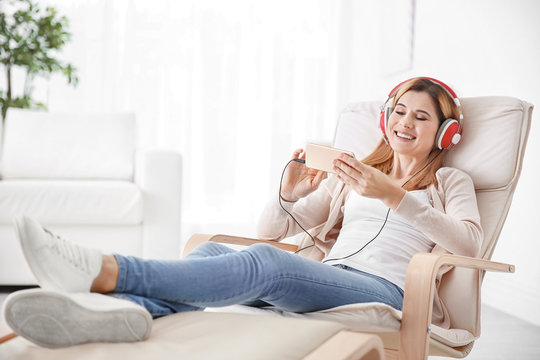 Young woman listening to music while relaxing in armchair at home