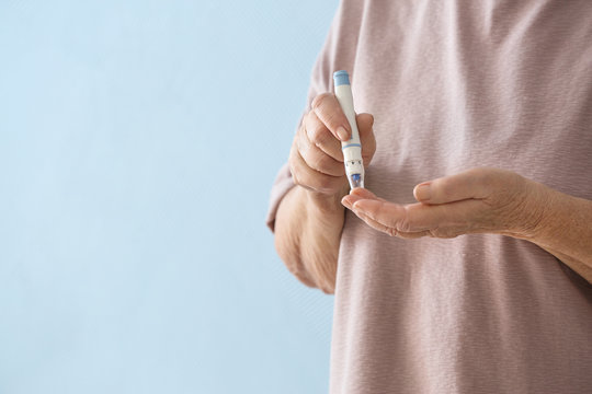 Elderly woman with diabetes measuring level of blood sugar on color background, closeup
