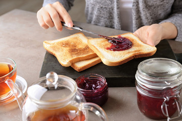 Woman spreading sweet jam on toast at table