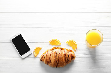 Tasty croissant, glass of orange juice and smartphone on wooden background