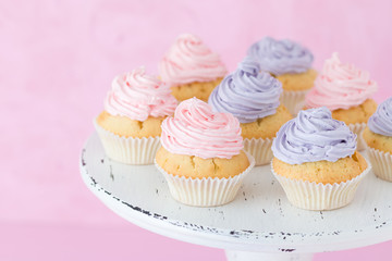 Cupcakes decorated with pink and violet buttercream on shabby shic stand on pastel pink background.