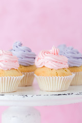 Cupcakes decorated with pink and violet buttercream on shabby shic stand on pastel pink backgroun