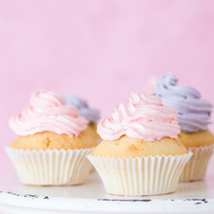 Cupcakes decorated with pink violet buttercream on shabby shic stand on pink pastel background.