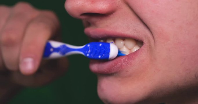 Handsome young guy (teenager) brushes teeth, green background.