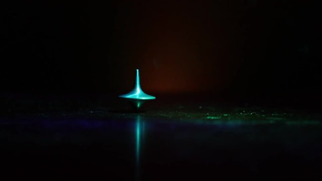 Totem spinning top spinning, wobbling and stopping. Spinning top on mirror surface with toned smoke background light. Whirligig in action in dark room on table. 