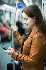 brunette girl using cell phone and smiling at subway