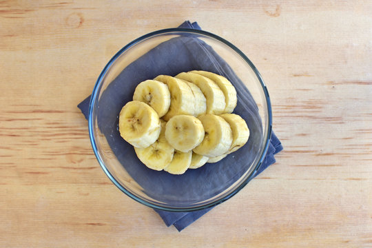 Sliced banana in glass bowl on wooden background.