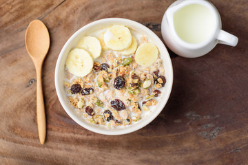 Muesli cereal with slice banana and milk in a bowl, top view