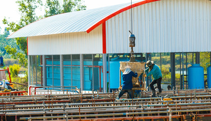 Group of construction workers pouring wet concrete using concrete bucket into the timber form work at the construction site.