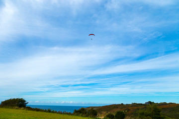 Fototapeta na wymiar Man Paragliding on a blue sky day day on a green european field with cliffs and the coast on the background