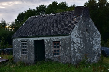 Weathered tiny country house on abandoned property in late evening light.
