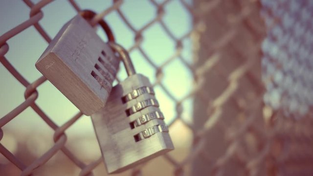 A metal lock sitting on a chain link fence in urban area