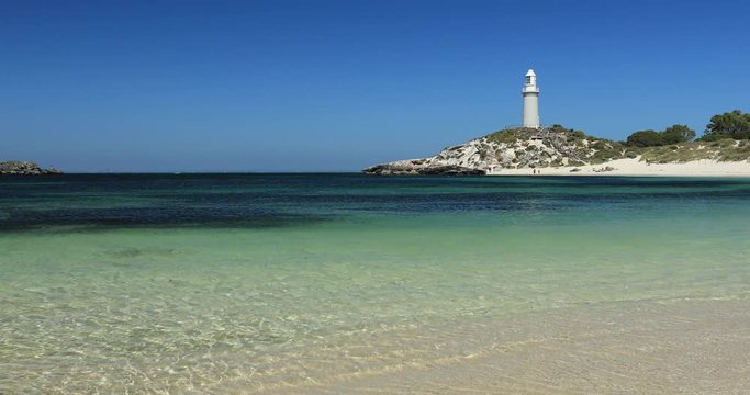 Ocean waves kiss the perfect white sand beaches of Rottnest Island, near Perth, in Western Australia. The Bathurst Lighthouse stands tall above the cliffs in the background.