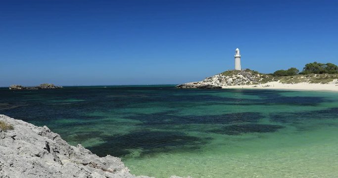 Ocean waves kiss the perfect white sand beaches of Rottnest Island, near Perth, in Western Australia. The Bathurst Lighthouse stands tall above the cliffs in the background.
