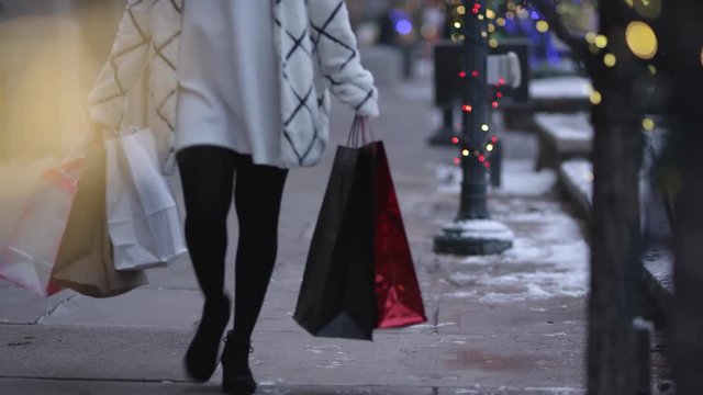 Woman christmas shopping carrying her bags down the sidewalk in front of shopping center.