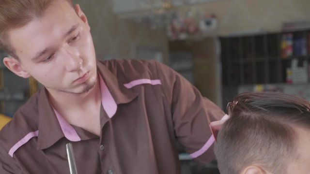 Close-up of barber cuts the hair by scissors at barbershop in slow motion.