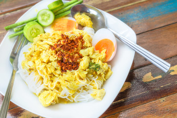 Rice vermicelli in green curry with Clown featherback, Clown knifefish and vegetables with Long bean and hoary basil on wooden table the traditional delicious Thai food.