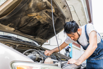 Fixing car engine in automobile repair garage. Handsome mechanics in uniform are repairing car while working in auto service