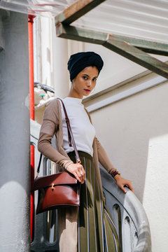 Image of a Muslim Malay woman looking self conscious and is posing in a relaxed way of going down the spiral step. SHe is wearing a navy blue hijab and a very classy outfit for the day.