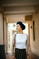 Portrait of a young Muslim woman wearing a hijab. She is standing in the midlle of the hallway and...
