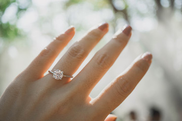 Close up of an elegant diamond ring on woman finger with blurry forest and sunlight background....