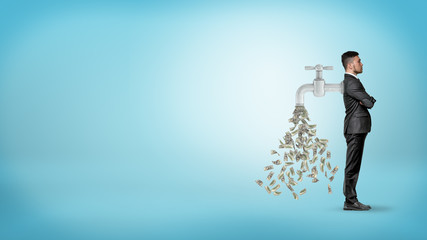 A businessman stands in a side view with a large faucet attached to his back and leaking money...