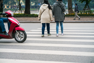 People walking across a street while motorbikes keep running on street in Hanoi, Vietnam. Closeup