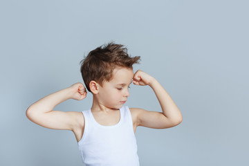 cute boy in white tank top tank top with fashion hair shows and looking at the biceps isolated on blue background