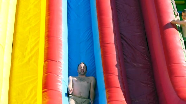 Slow motion a man sliding down big inflatable slide during a party